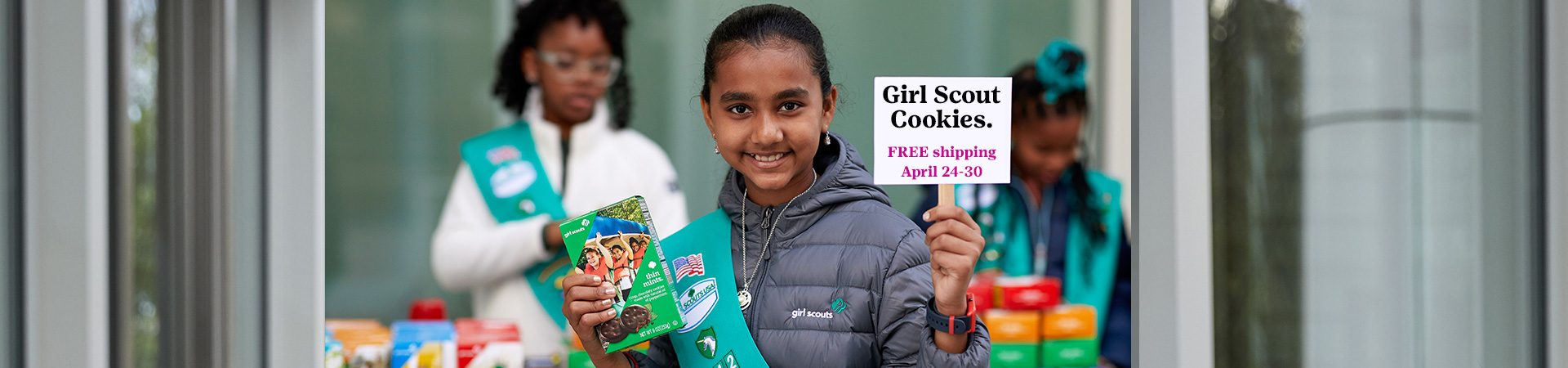  girl scouts selling cookies with one girl in front of booth holding sign that says "girl scout cookie proceeds stay local" 