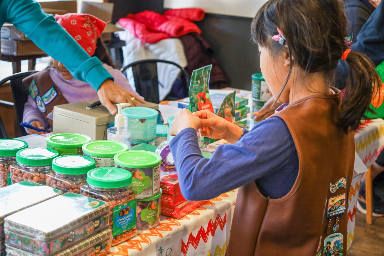 volunteer with junior girl scouts at outside cookie booth smiling