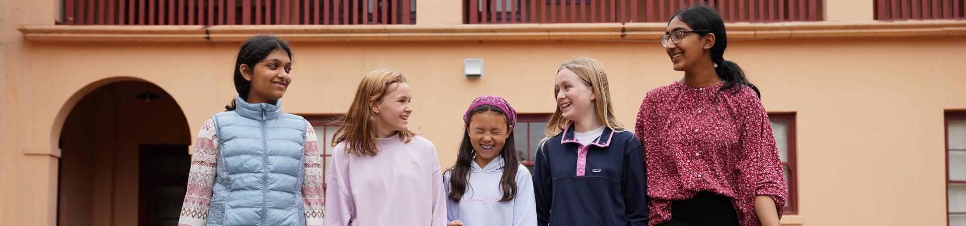  group of junior girl scouts walking outside hugging smiling at camera in junior vest and sash with badges 