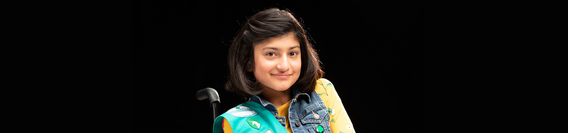  High school girl in Girl Scout sash and winter jacket smiling at camera against green backdrop. 