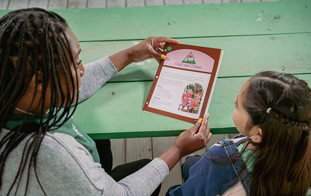 adult volunteer and girl scout sitting at table looking on phone at digital resources