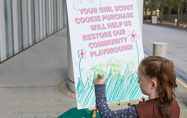 volunteer with junior girl scouts at outside cookie booth smiling