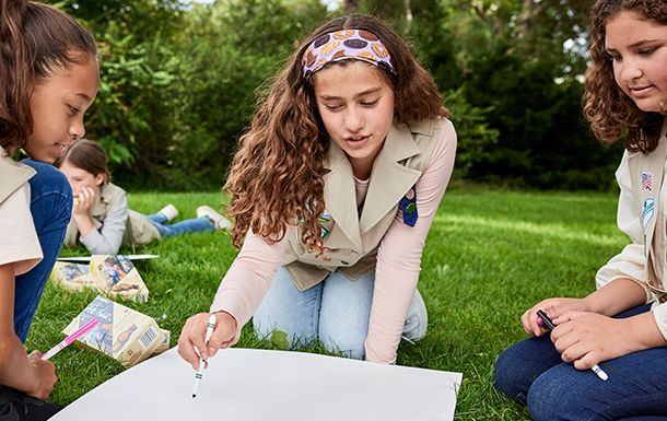 volunteer with junior girl scouts at outside cookie booth smiling